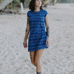 Lady looking out to sea, walking on the beach under palms, wearing a electric blue handloomed cotton shift dress. Above knee, round neck. 