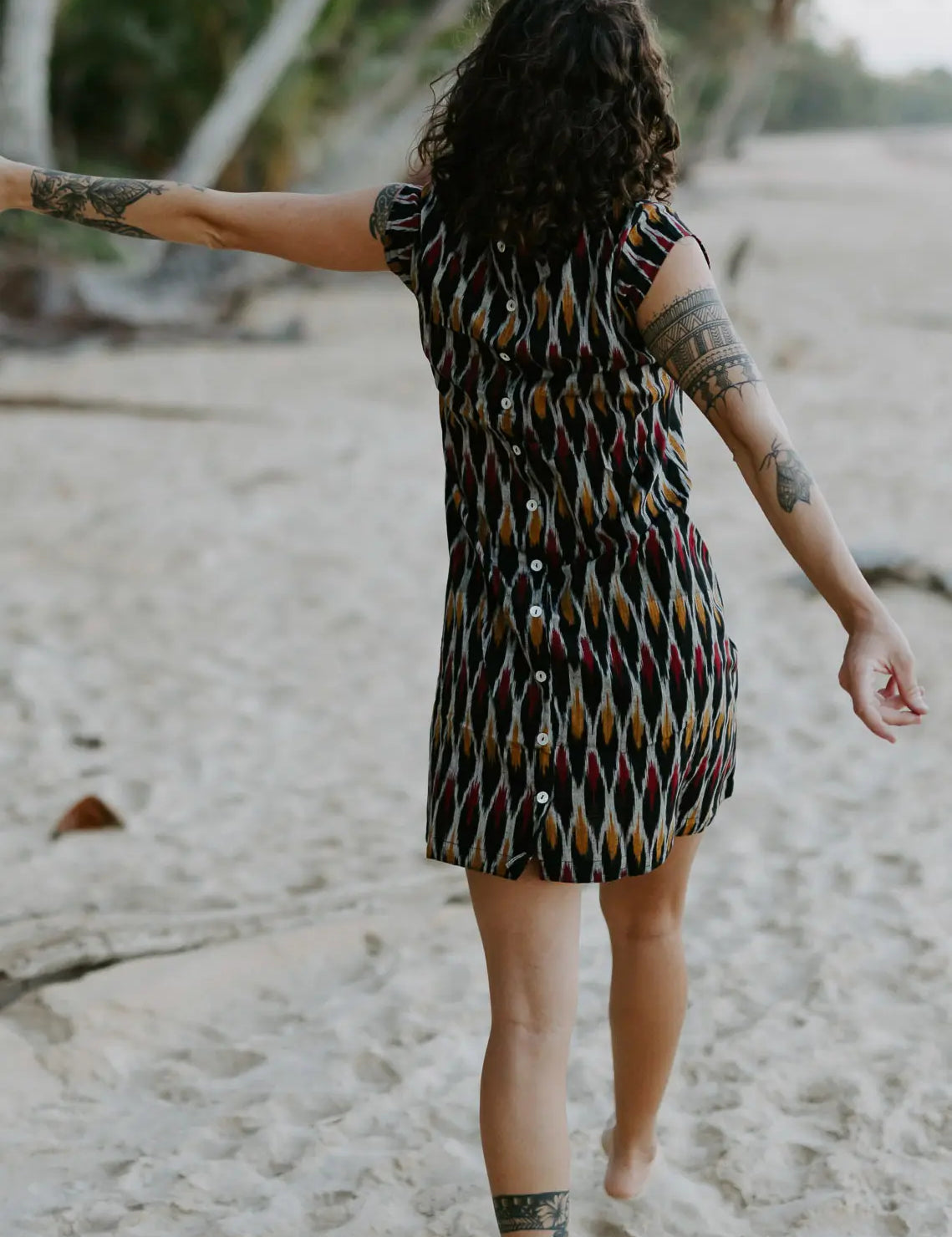 Woman walking in the sand under palm trees wearing a Vibrant short dress crafted from handloomed Ikat cotton