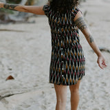 Woman walking in the sand under palm trees wearing a Vibrant short dress crafted from handloomed Ikat cotton