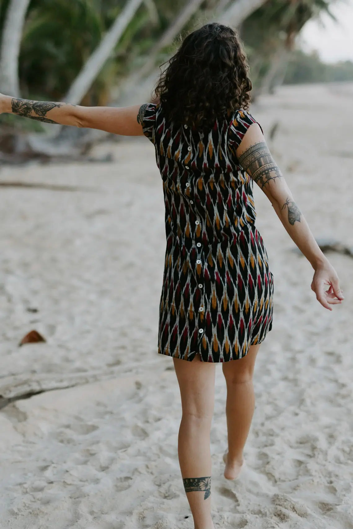 Woman walking in the sand under palm trees wearing a Vibrant short dress crafted from handloomed Ikat cotton