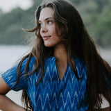 Woman wearing a blue Ikat cotton dress with a V-neckline, walking along the shoreline, showcasing artisan makers of handwoven fabric