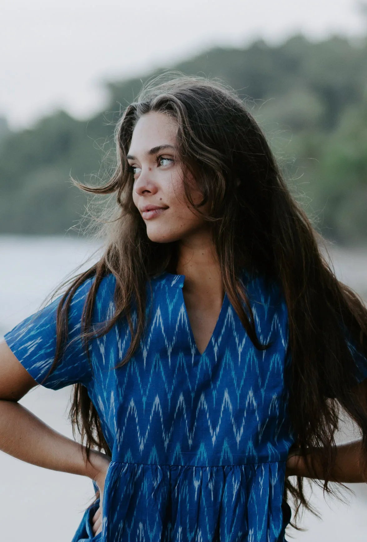 Woman wearing a blue Ikat cotton dress with a V-neckline, walking along the shoreline, showcasing artisan makers of handwoven fabric