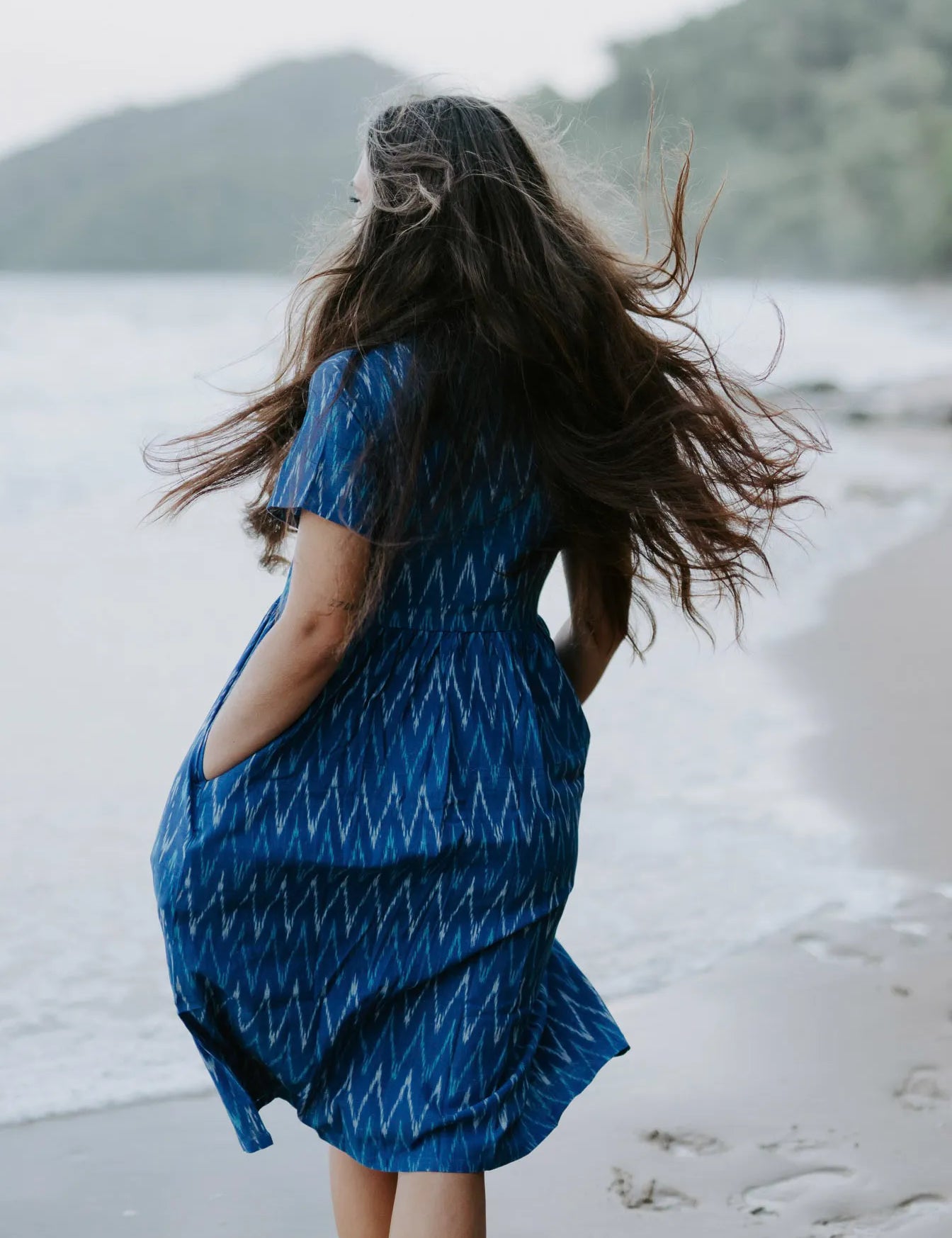 Blue Ikat cotton dress worn by a woman on the beach, highlighting its lightweight, sustainable design and artisan craftsmanship.