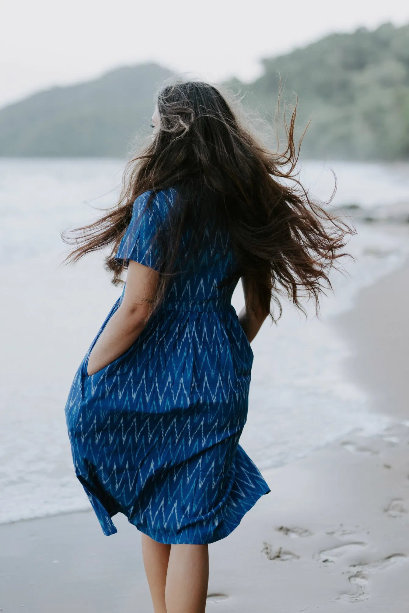 Blue Ikat cotton dress worn by a woman on the beach, highlighting its lightweight, sustainable design and artisan craftsmanship.