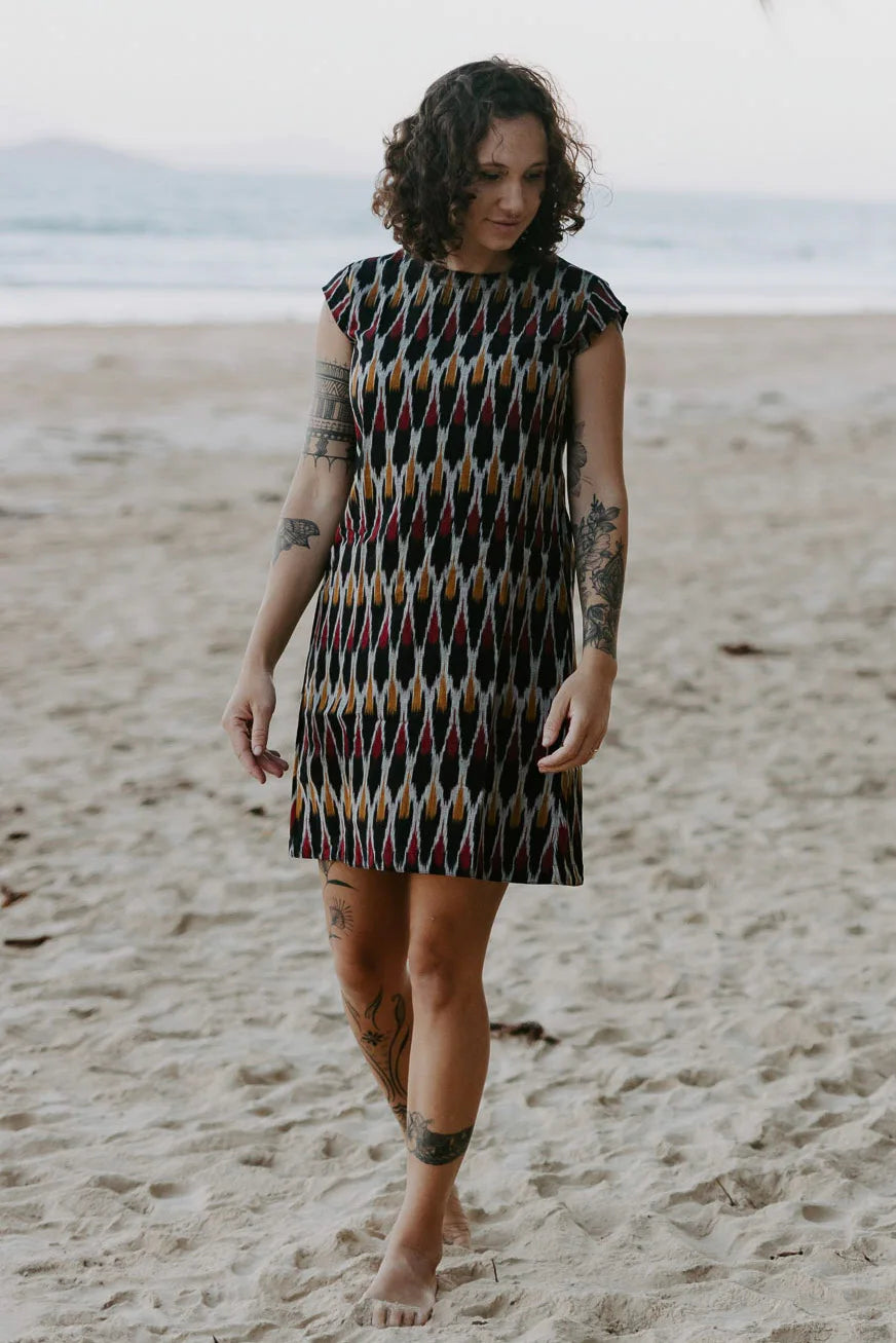 Red, mustard, and black artisan shift dress styled on the beach. 