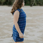 Ethically crafted electric blue cotton dress for all-day comfort. Woman looking away into the distance at beach. Palm covered shore line