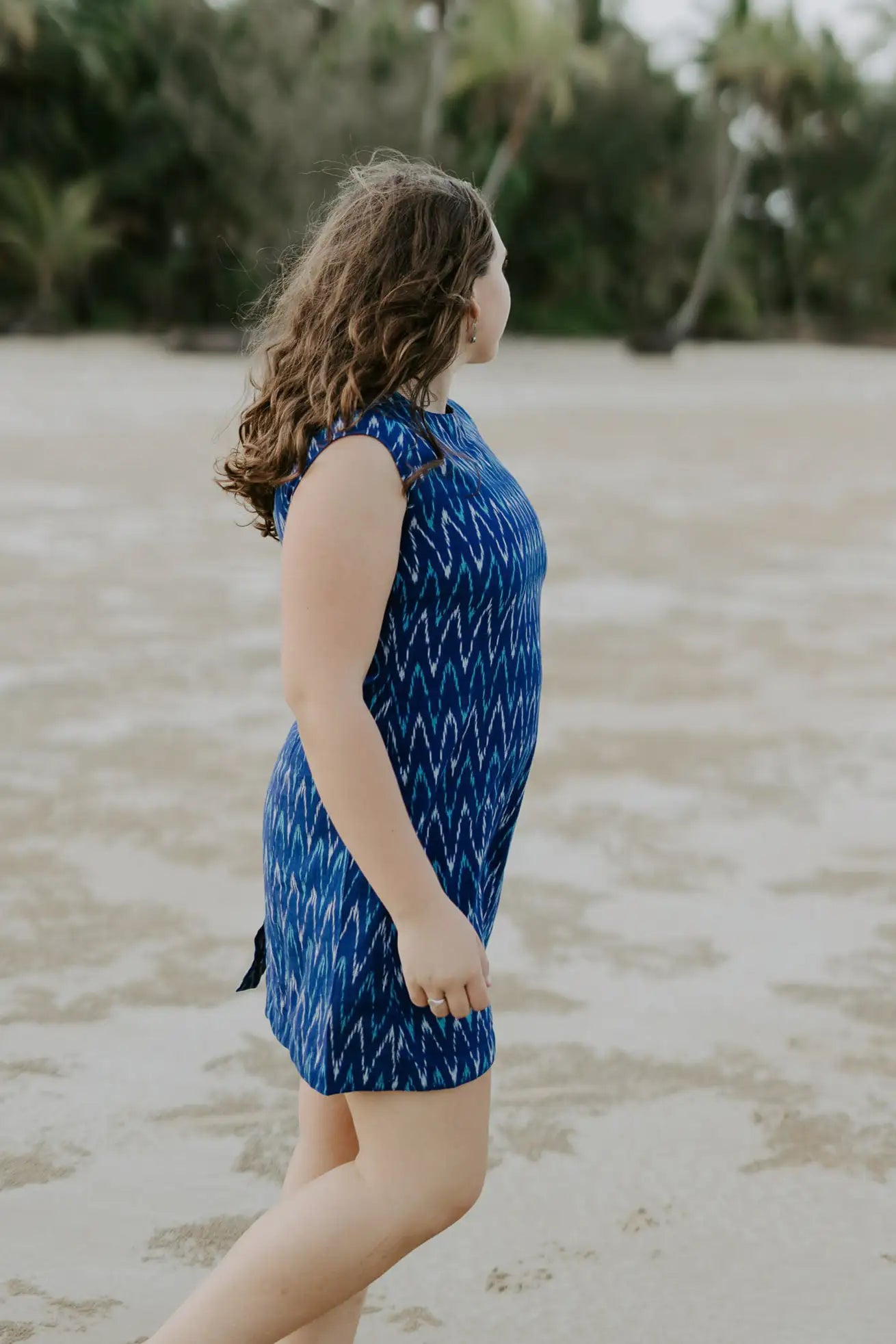 Ethically crafted electric blue cotton dress for all-day comfort. Woman looking away into the distance at beach. Palm covered shore line