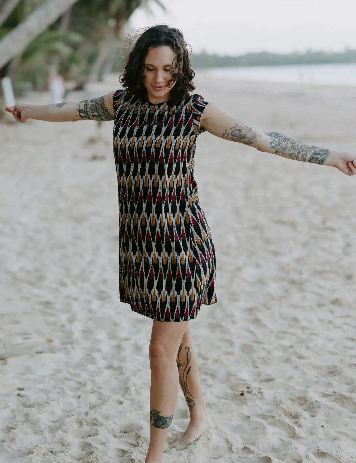 Woman walking on the beach wearing the Tara Shirt Dress in red, mustard, and black Ikat