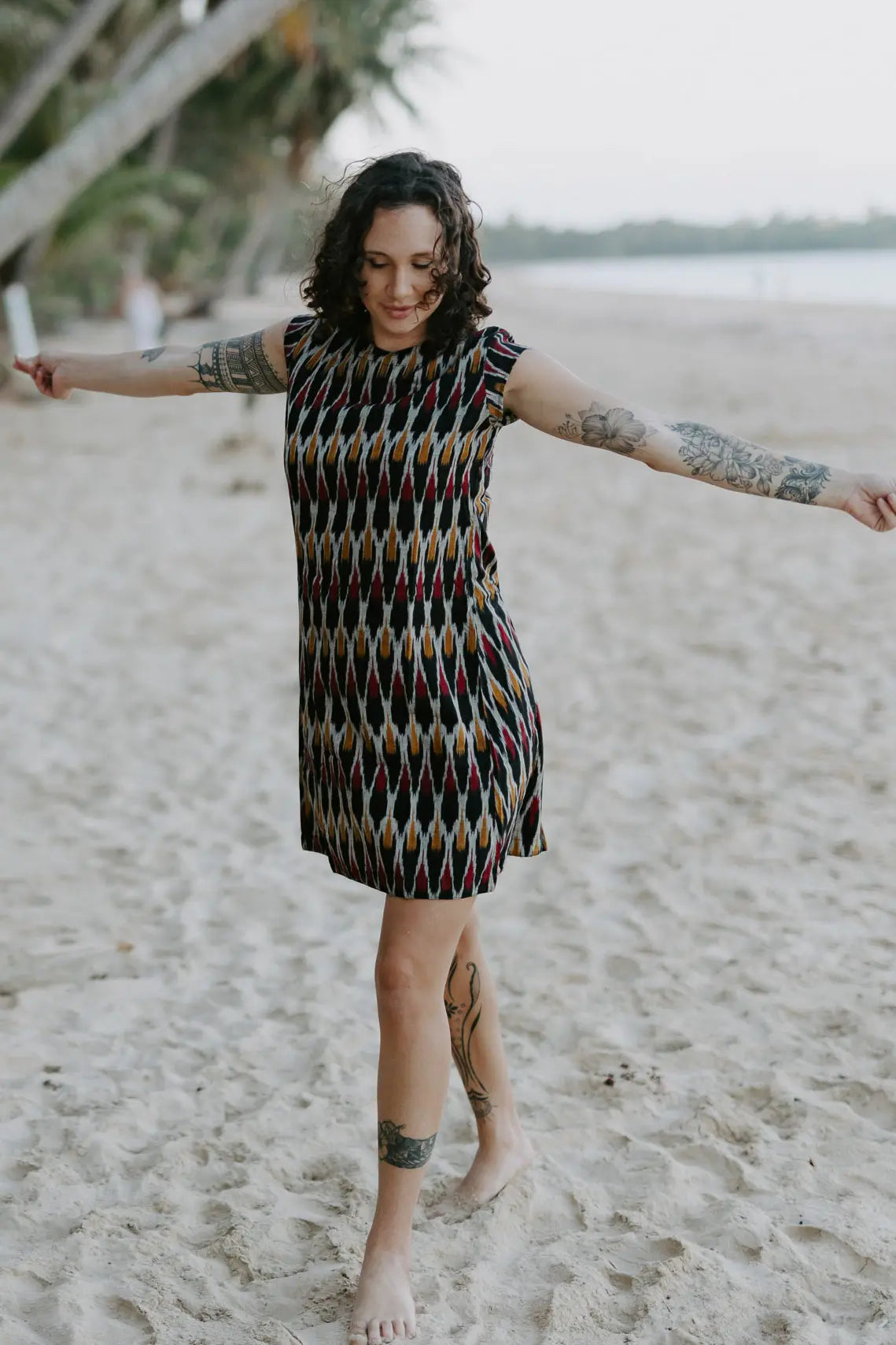 Woman walking on the beach wearing the Tara Shirt Dress in red, mustard, and black Ikat